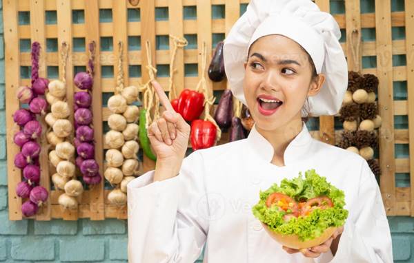 a woman in chef uniform holding a bowl of salad